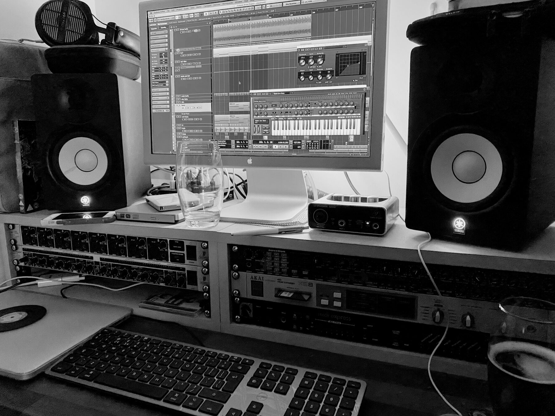 Black and white photo of a desk with racks of outboard gear, laptop and monitors