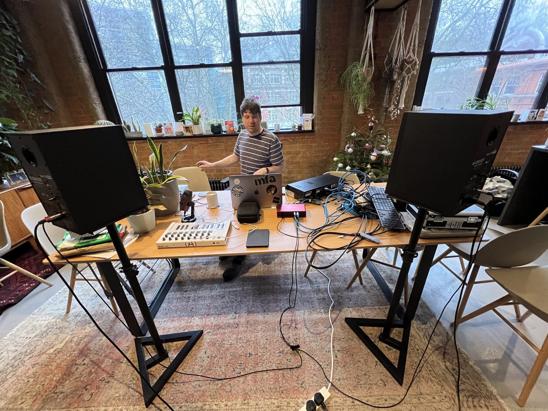 A bright loft room with a desk, speakers on stands, plants and tall windows